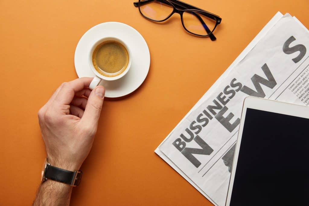 a coffee cup next to a business news section. Being aware of inflation helps you know how to lower your medication costs.