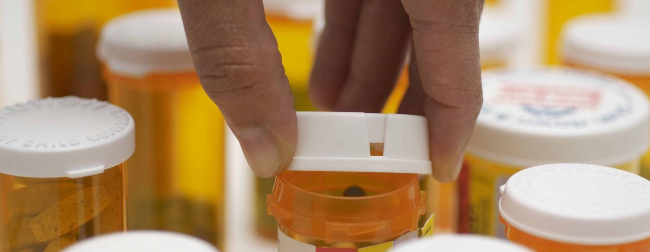 Man's hand opening pill bottle, close-up