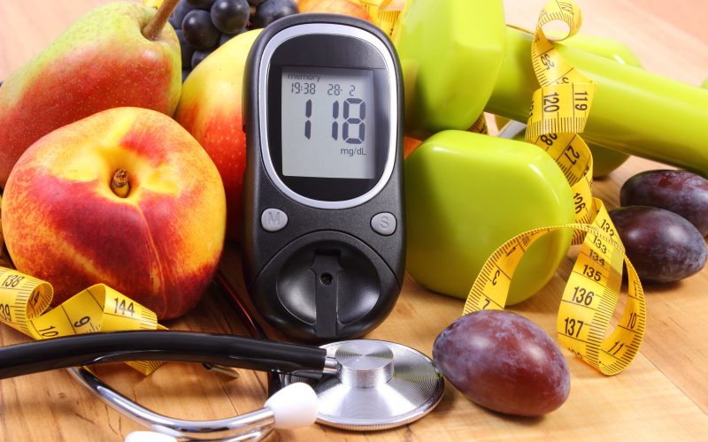 Glucose meter with medical stethoscope, fruits and dumbbells for using in fitness, concept of diabetes, healthy lifestyles and nutrition