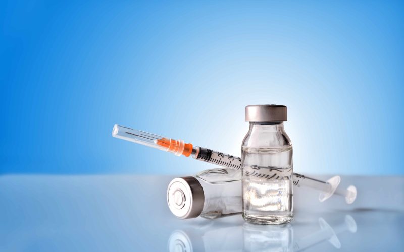 Vials with medication and syringe on white methacrylate table with blue background. Horizontal composition. Front view.