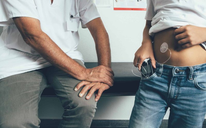 Cropped view of a young diabetic patient is keeping in his pocket an insulin pump in the doctor office. Child diabetes concept