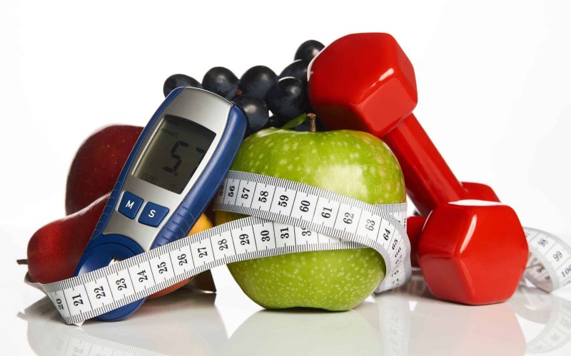 Blood sugar control glucometer for glucose level with healthy organic food and dumbbells with measuring tape on a white background. Healthy lifestyle, detox, weight loss and Diabetes concept