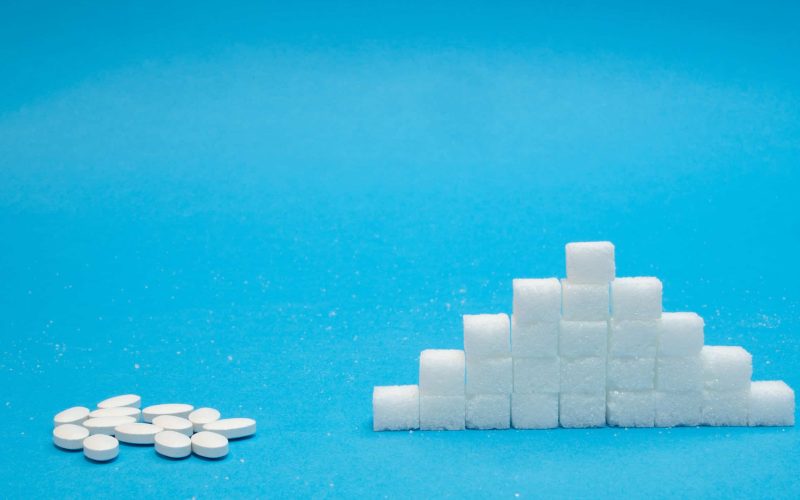 small pills of sugar replacement vs neat pile of refined sugar. natural vs chemical concept on blue background