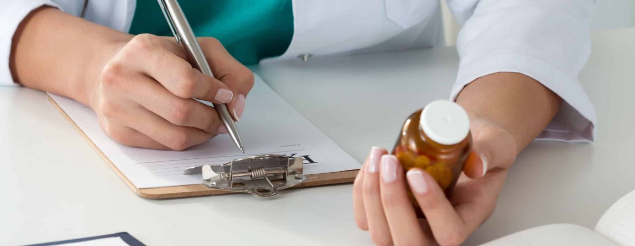 close-up of doctor's hands writing prescription and holding bottle with pills. healthcare, medical and pharmacy concept.