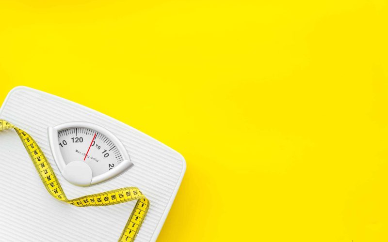 Diet. Bathroom scales and measuring tape for weight loss concept on yellow background top view mock up