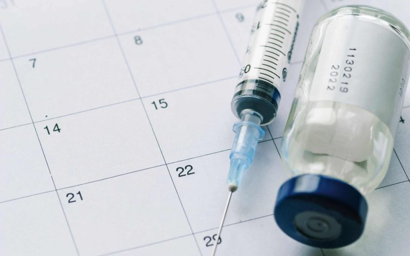 The vial with vaccine and syringe on calendar background, as a concept of vaccination season and date.