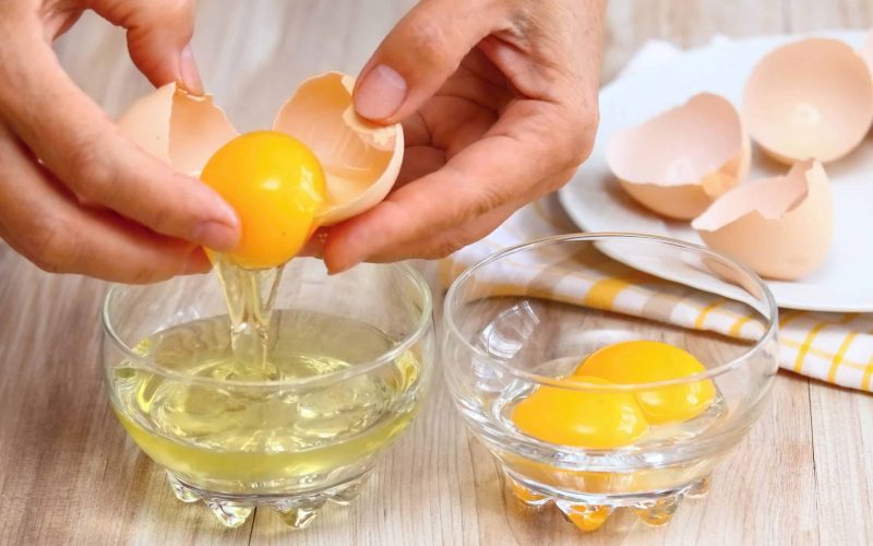 61227425 - woman hands breaking an egg to separate  egg- white and  yolks and egg shells at the background