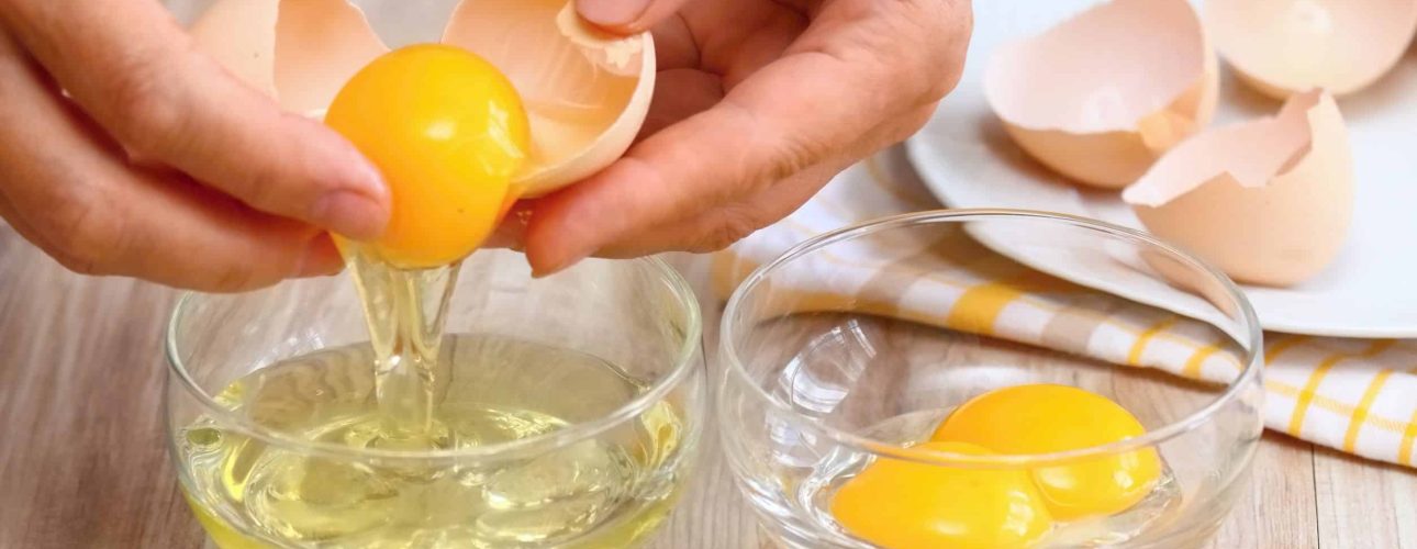 61227425 - woman hands breaking an egg to separate  egg- white and  yolks and egg shells at the background