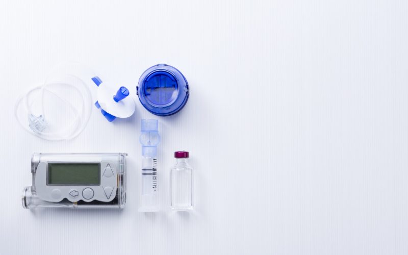 top view of an insulin pump set background consisting of: an insulin pump, insertion system of the infusion set, a reservoir of a insulin pump, insulin vial and a infusion set on a white background