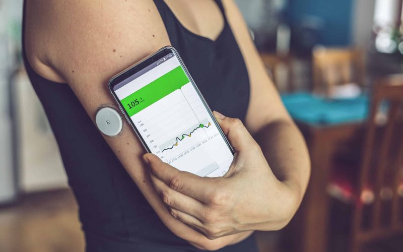 Woman checking glucose level with a modern technology remote sensor and mobile phone, without blood. Diabetes treatment.