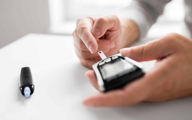 medicine, age, diabetes, health care and old people concept - senior man with glucometer checking blood sugar level at home