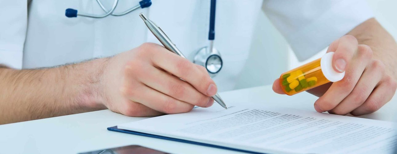 Close up of male doctor writing prescription paper and capsules