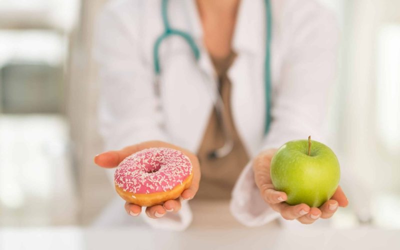 Closeup on medical doctor woman giving a choice between apple and donut