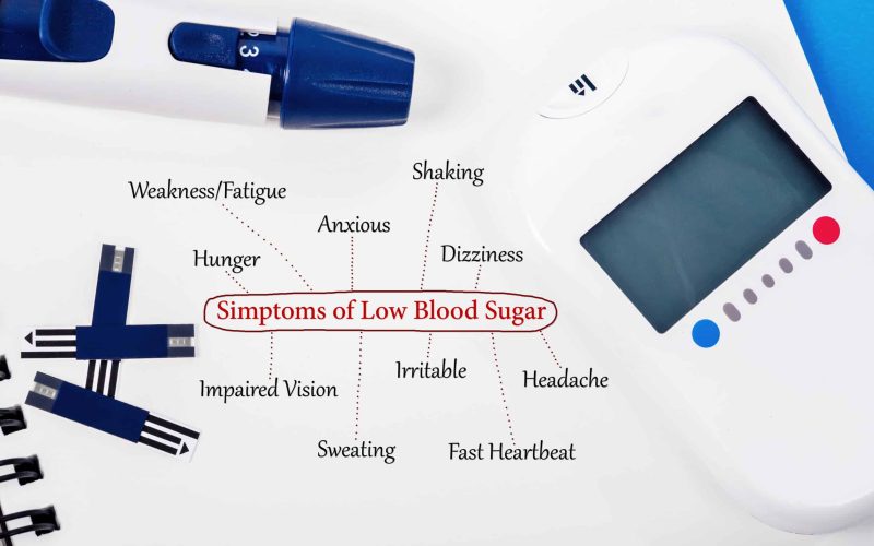 Symptoms of low blood sugar with blood glucose meter and equipment on book background.