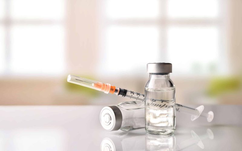 Vials with medication and syringe on white methacrylate table with window background. Horizontal composition. Front view.