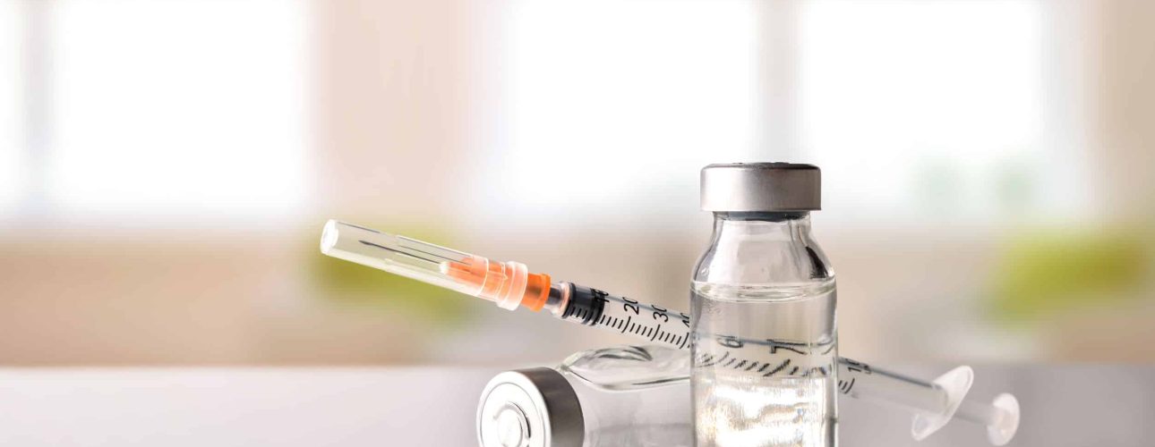 Vials with medication and syringe on white methacrylate table with window background. Horizontal composition. Front view.