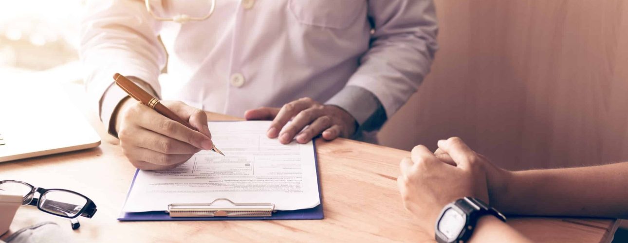 Doctor hand holding pen writing patient history list on note pad and talking to the patient about medication and treatment.