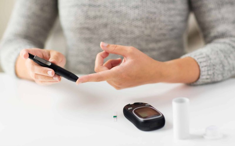 medicine, diabetes, glycemia, health care and people concept - close up of woman checking blood sugar level by glucometer at home